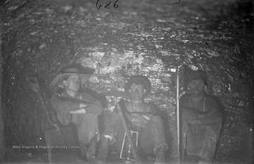 Three unidentified coal miners are pictured inside a mine with shovels and an oil lamp.