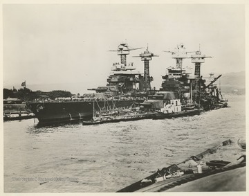 "This port quarter shot of the W. Va. taken from the capsized Oklahoma, shows a general view of the damage to the W. Va., sunk in the Japanese raid on Pearl Harbor, Dec. 7, 1941."The U.S.S. Tennessee is visible behind the sunken U.S.S. West Virginia.  Part of the U.S.S. Oklahoma is visible in the foreground.