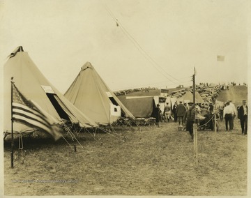 Tents of the Ohio and Pennsylvania realms are pictured on the left. In the background, dozens of cars are parked on a field where men and women walk around. 