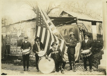 Five African-Americans with drums and a large American flag pose for a group photo. The posters in the background are for Richards the Wizard, who was an active magician touring from 1910-1930.