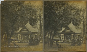 A man sits on a chair in the lawn. In the background is a small pavilion. The stereograph is part of photographer William Dunnington's "Webster Springs Series."
