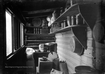 View of a small pantry room, storing various canned foods and supplies. In the background, on the top shelf, is a barrel that has "Mr. T. B. Green" burned into the wood. Mr. T. B. Green refers to Thomas B. Green (b. 1853, d. 1940/01/27), father of photographer James Edwin Green, Sr., and grandfather to James Edwin Green, Jr. 