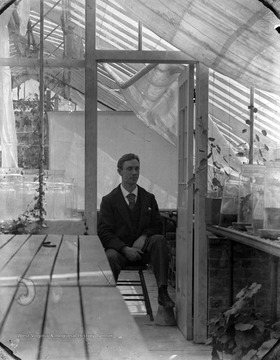 Rumsey was an entomologist and photographer. He is pictured in what appears to be a greenhouse. There are several plants and jars surrounding Rumsey, perhaps because of his insect studies. 
