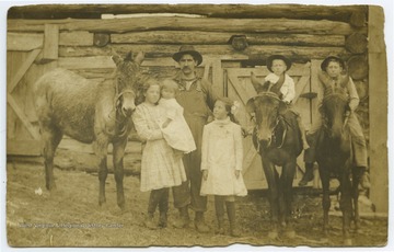 A man put his arms around his three daughters. On the right of him, his two sons sit on mules. These are likely relatives of the Lewis family. 