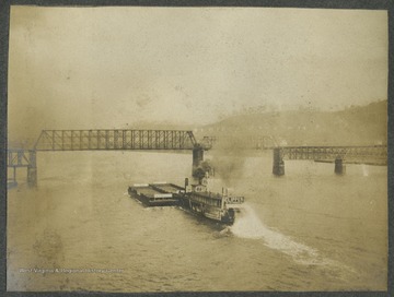 A steamboat travels down the river. The railroad bridge is pictured in the background.This photograph is found in a scrapbook documenting the survey for the Baltimore and Ohio Railroad in West Virginia and surrounding states. 