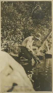 A man uses a washboard to wash clothing in the river.This photograph is found in a scrapbook documenting the survey for the Baltimore and Ohio Railroad in West Virginia and surrounding states. 
