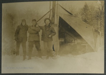 Three men pose outside of a tent which has a "comfortable" interior, as described the photograph's inscription.This photograph is found in a scrapbook documenting the survey for the Baltimore and Ohio Railroad in West Virginia and surrounding states. 