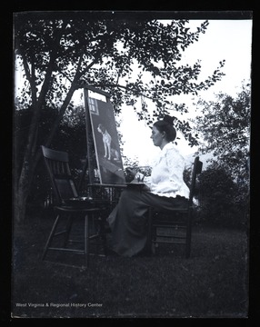 A woman sitting outside painting a picture of a dog.