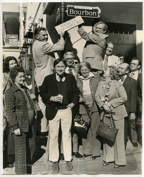 "A group of West Virginians, crowded around a Bourbon Street lamp post as the city observed 'West Virginia Day.' State Sen. Carl Gainer, top left hands a sign changing Bourbon Street to 'West Va. Country Road.'"