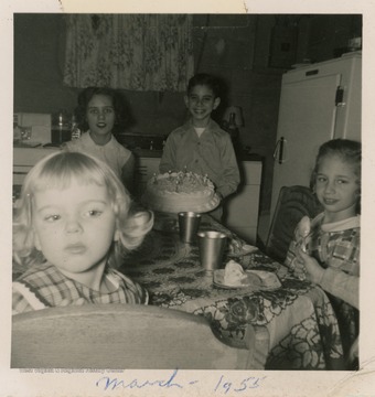 One of the three children holds a birthday cake.