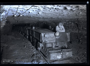 Man poses on top of engine hauling loaded coal cars.