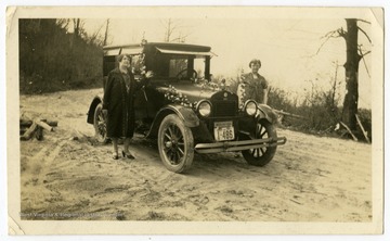 Two women pose by their 1927 model car, which is decorated with flowers.