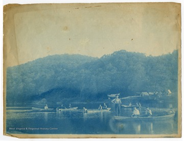 A group of men pend time in boats on the Cheat River. The banner in the background reads in part, "Elkhorn Hunting."