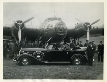 President Roosevelt is shown posing in the presidential limousine in front of officers and an army aircraft with Assistant Secretary of the Navy Charles Edison (back of middle seat) and the Assistant Secretary of War Louis Johnson (beside Edison), among others. The president inspected aircraft at the Army's Bolling Field and the Naval Air Station. 