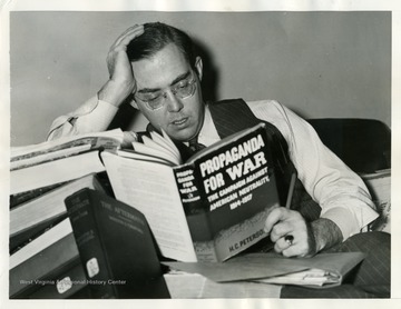 Text on back reads, "Washington D. C.: Senator Rush Holt, of West Virginia, is shown buried in the pile of books he used in gathering material for his speech on the Senate floor, in Washington, D. C., where debate on the administration's neutrality bill is in its third week. The senator said repeal of the arms embargo was not necessary for "cash-and-carry" trade between the United States and belligerents in other commodities. The neutrality act 'was written for the defense of the United States, not for defense of Great Britain, France, or Germany,' said the senator." 
