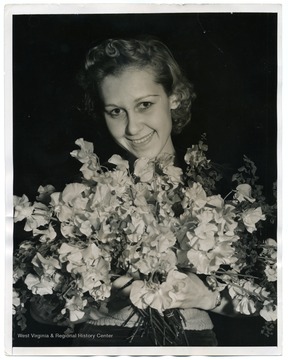 Text on back reads, "New York: Miss Florence Stevens, of New York, shown with the new sweet pea "Pearl Buck," named in honor of the Nobel Prize winner and developed by Davis Burpee, Philadelphia hybridist, which is on exhibit at the International Flower Show in New York. It is a clear salmon pink with unusually large flowers."