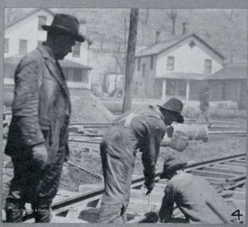 Photograph from "The Hardwood Bark," a periodical journal published by the W. M. Ritter Lumber company in the interest of its employees.This image is on a page with several other photos titled "Snapshots From Hurley." The caption for this photo reads:"4. Frank Crockett superintending the track laying at the ney Hurley Machine Shop. The two ment at work on the track are E.M. Thomas and Bud Estep."