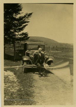 Charles Skidmore Harper sitting on the front of his car.