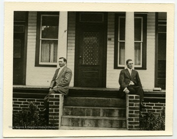 Two men sit in front of a home used by the Hatfield family.