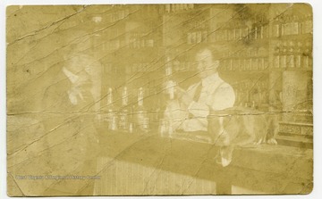A postcard picture of John Caldwell in Elias Hatfield's Saloon. A dog sits on the counter.